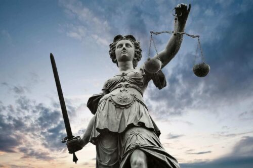Majestic statue of Lady Justice holding scales and sword against a dramatic sky, symbolizing fairness and authority in the legal system.